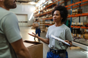African American warehouse worker discussing about delivery schedule with her coworker.