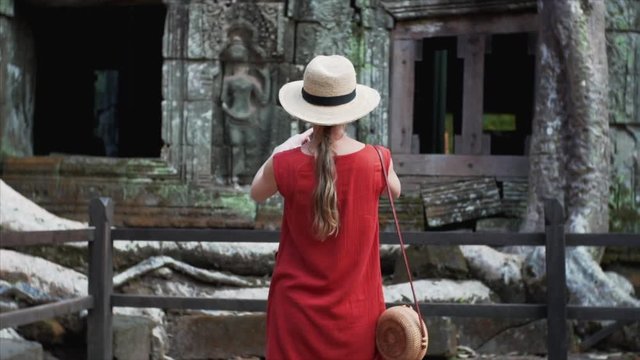 Slow motion. Caucasian woman in straw hat is exploring Ta Prohm temple and taking photo of giant banyan roots growing on its gallery. Cambodia