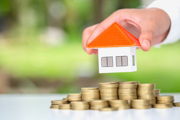 Human hand putting house model on coins stack,  planning savings money of coins to buy a home...