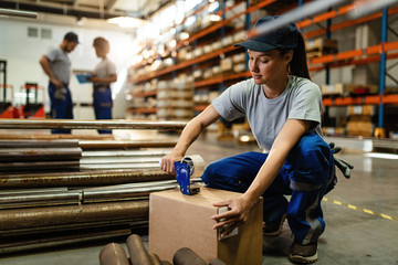 Female warehouse worker taping cardboard box with tape dispenser before the shipment.