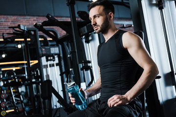 Fototapeta na wymiar low angle view of handsome sportsman in sportswear holding sport bottle in gym
