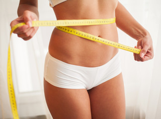 Hands measuring waist with a tape. Slim and healthy woman at her home