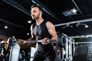 low angle view of athletic man exercising with heavy barbell in gym