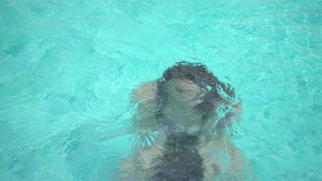 Asian young mother and little baby girl having fun in a swimming pool. Mom is teaching her daughter to dive in the pool. Happy family concept.