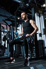 Fototapeta na wymiar low angle view of sportsman in sportswear holding sport bottle in gym
