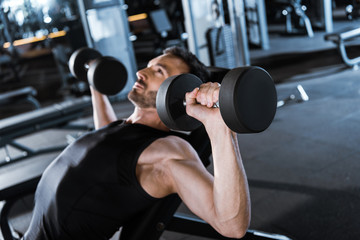 selective focus of bearded man working out with dumbbells in gym
