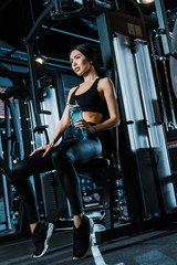 Fototapeta na wymiar low angle view of attractive sportswoman in sportswear holding sport bottle in gym