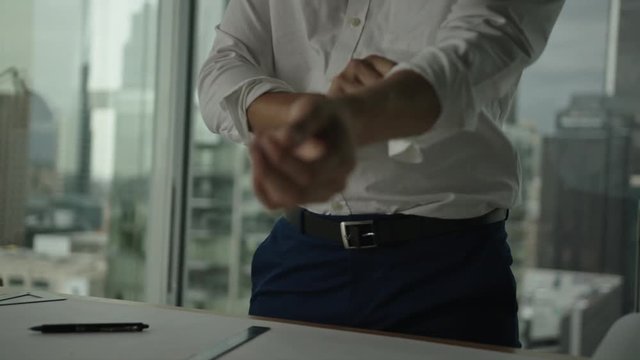 Businessman rolls up sleeves and starts to work on blueprint in office with view on downtown and skyscrapers. Architect's work process.