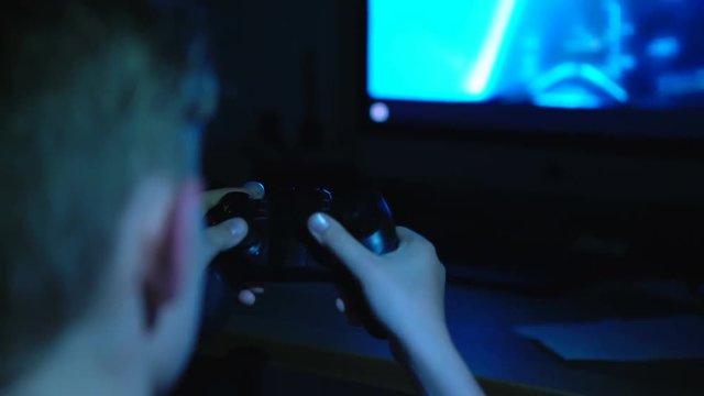 4K Boy playing video games sitting in darkness with joystick in his hands