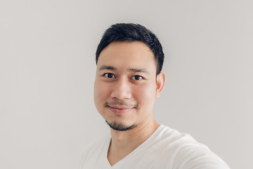 Smile man is taking selfie of himself with white t-shirt and grey background.