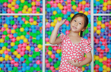 Fototapeta na wymiar Beautiful Asian little girl doing thai style dance expressions against colorful toy ball playground. Expresses pleasant emotions.