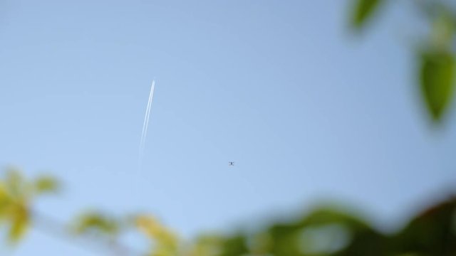 Drone Flying In The Blue Sky With A Plane In The Background From The Ground in france in slowmotion with plants in the foreground with bokeh