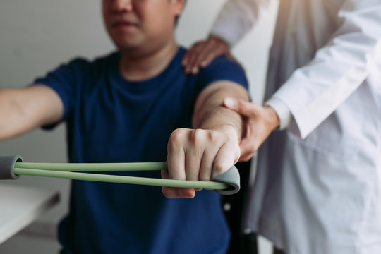 Asian male physical therapist descent working with patient doing stretching exercise with a flexible exercise band in clinic room.