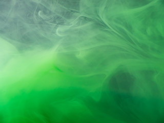 Green acrylic paint dissolving into water, abstract pattern. Close up view. Blurred background. Acrylic smoke under water, abstract background. Paint in liquid. Abstract art for wallpapers