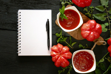 tomato sauce.Homemade tomato ketchup Homemade tomato ketchup, large  red tomatoes with leaves, white blank notebook on a black wooden background. Tomato Sauce Recipe
