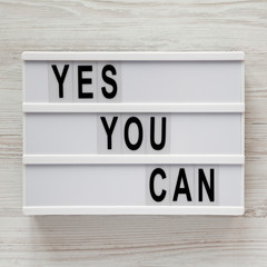 'Yes you can' words on a light box over white wooden surface, top view. Overhead, from above. Flat lay. Close-up.