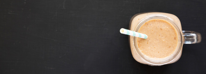Banana apple smoothie in a glass jar over black surface, top view. Flat lay, from above, overhead. Copy space.