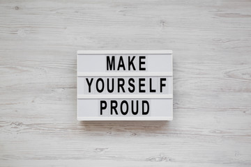 'Make yourself proud' words on a light box over white wooden background, overhead view. Flat lay, top view, from above. Close-up.