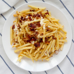 French fries with cheese sauce and bacon on a white plate, view from above. Flat lay, overhead, top view.