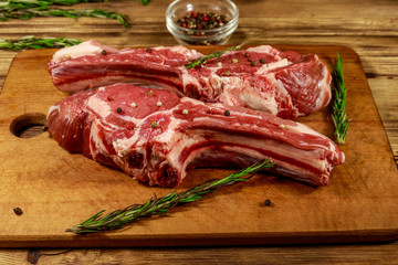 Raw fresh beef rib eye steaks on bone with spices and rosemary on wooden table
