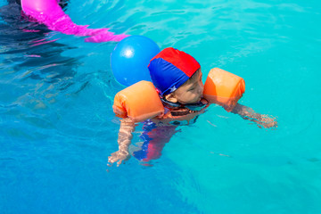 Little boy child in swimming suit with orange sleeve floats in the pool