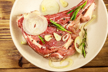 Marinated beef rib eye steak on bone with spices, onion and rosemary on wooden table