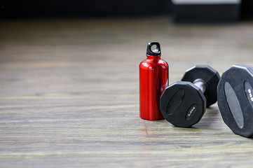 Black dumbbell and red bottle on wooden floor with copy space, fitness and healthy concept.