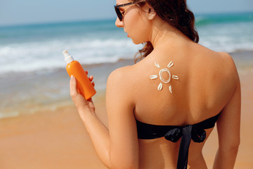 Skin care.Sun protection. Beautiful woman in bikini apply sun cream on Face. Woman with Suntan lotion on beach. Portrait of female holding moisturizing sunblock. The girl uses sunscreen for her skin
