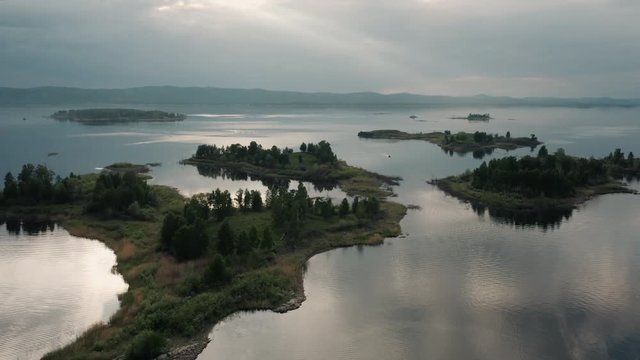 Aerial view; drone flying forward over flooded terrain with uninhabited island and wild flora and founa; untouched nature national in park in Ural; sunset evening time; boat trip between curved coasts