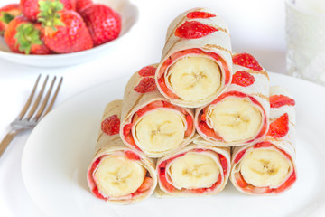 Vegetarian strawberry banana rolled pancakes in shape of pyramidon white background