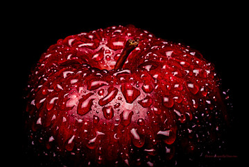 A Frame filling Macro image of a vibrant Red apple covered in water drops beading on the peel.  This is a high contrast image with a strong highlight on the front of the fruit.