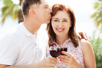 A middle aged man and woman hold glasses of wine against the backdrop of the tropics.