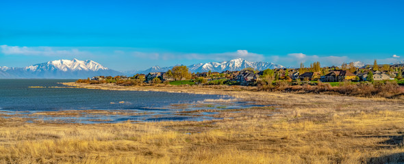 Houses in front of a lake with grassy shore and glittering water on a sunny day
