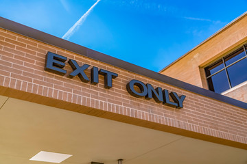 Exit only sign on the exterior brick wall of a building with shiny window