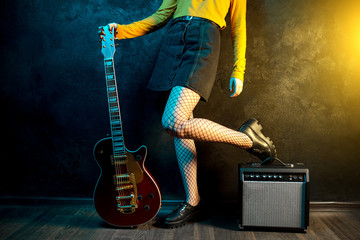 Close-up photo of young hipster woman legs and red guitar in neon lights. Rock musician is playing...