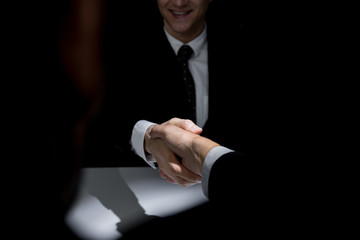 Business partners making handshake in dark shadow