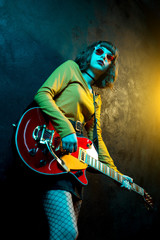 Beautiful young hipster woman with curly hair with red guitar in neon lights. Rock musician is...