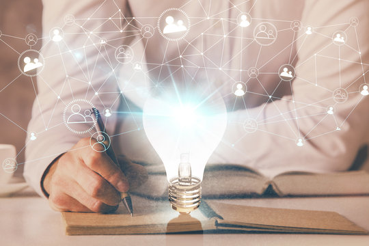 View of Bulb lamp idea concept icon on a futuristic interface with writing man's hand background. Double exposure.