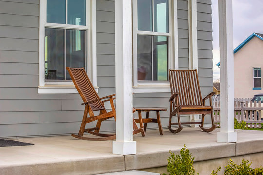 Front porch of a house with brown rocking chairs and rectangular white pillars