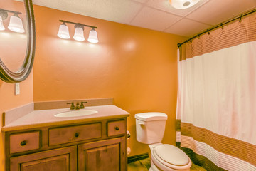 Toilet and vanity with wooden cabinet and round mirror inside a bathroom