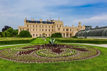 Lednice, Czech Republic - May 28 2019: Famous Lednice castle in South Moravia with yellow facade. Garden with green lawn, flowers and sand footpath. Sunny spring day, blue sky, white clouds.