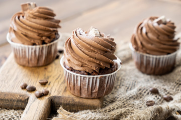 brown cupcakes with cocoa cream, cinnamon and coffee on wooden background