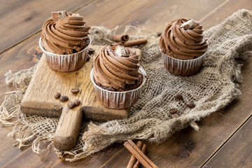 brown cupcakes with cocoa cream, cinnamon and coffee on wooden background