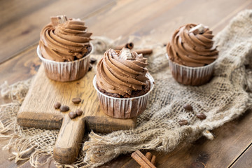 brown cupcakes with cocoa cream, cinnamon and coffee on wooden background