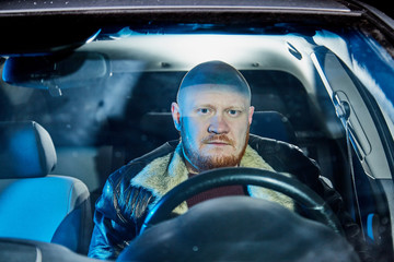 Male driver in a leather jacket in the car in the dark. Night photo shoot