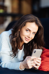 Pretty young girl using her smartphone on couch at home in the living room