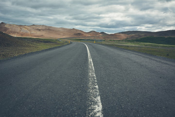 View to the empty road, empty meadow and red mountains in the background in Myvatn region, overcast day in summer, vintage effect with grain