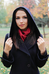 The girl in the black coat looks away from the camera on background of autumn trees.