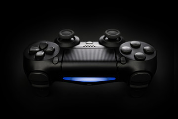 Closeup photo of video game console gamepad joystick controller on black background with blue light.