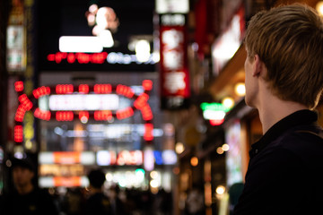 A young tourist looking off to the distance in a neon lit Tokyo street